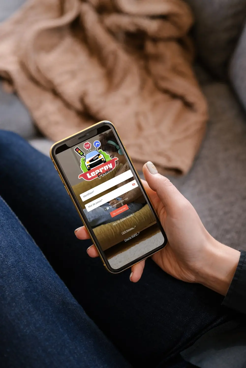 Femme utilisant l’application mobile Learny Permis sur smartphone depuis son canapé.